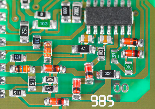 Closeup a surface mount assembly of electronic components on printed circuit board. Red or orange Zener diodes, black micro chip and small resistors or capacitors on green PCB detail. Electrotechnics.