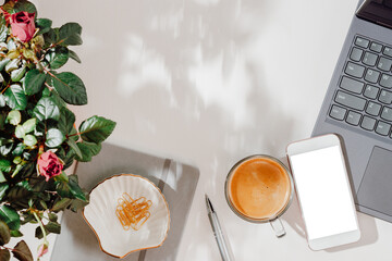 Sunny home office background with smartphone mockup, laptop, coffee and rose house plant, aesthetic shadows, copy space for design, girlish workspace