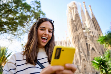 Young women friend using mobile phone in hands in front of Sagrada Familia in Barcelona. Beautiful...