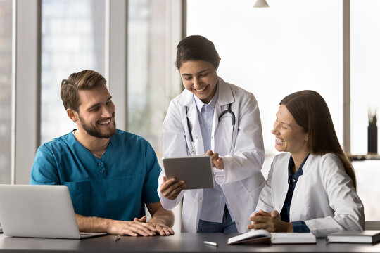 Three multiethnic medical worker using modern digital tablet device at workplace, sharing humorous, positive moment at break, read good news related to patient progress or successful treatment outcome