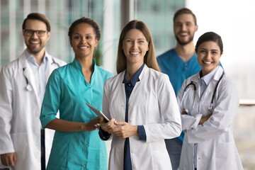 Group of five healthcare professionals, doctors and nurses looking at camera with friendly smile....