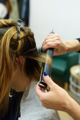 Fototapeta premium Hairdresser straightening woman's hair with hair straightener in salon