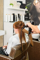 Hairdresser drying woman's hair with hairdryer in barber shop