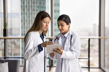 Young women healthcare professionals using tablet, look at device screen, reviewing patient...