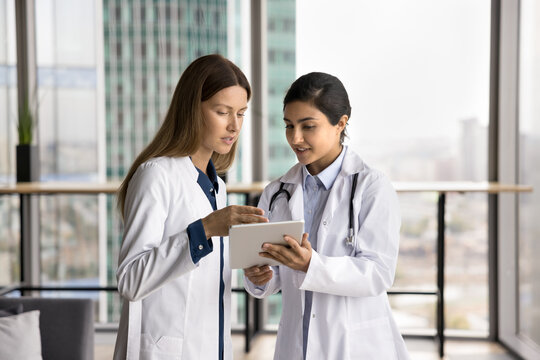 Young women healthcare professionals using tablet, look at device screen, reviewing patient records, analyze medical x-rays images, discuss diagnosis, planning treatment options, read medical research