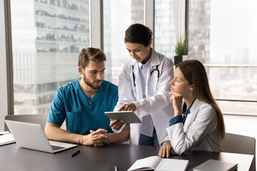 Three multinational doctors working using digital tablet, talking, reviewing patient electronic...