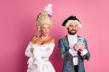 Elegant couple in historical costumes posing against a pink background for a thematic photoshoot showcasing romance and playful humor