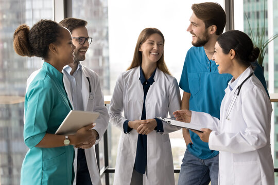 Group of nurses, doctors gathered together standing in clinic office, laughing, take break, engaged in briefing, joking, looking happy, take part in friendly conversation before workday. Collaboration