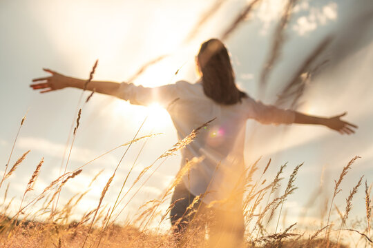 Woman enjoying the sun feeling joyful with open arms standing in a field - Powered by Adobe