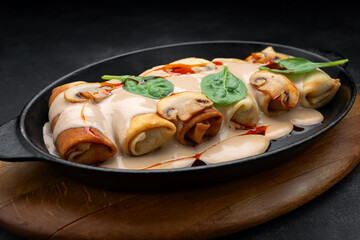 Pancakes with mushrooms, sauce and spinach, in a frying pan