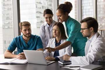 African medical worker in green scrubs explain opinion to her colleagues using laptop points on screen to x-ray result that shows information related to patients diagnosis, injury, or treatment plan