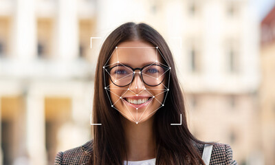 A woman with glasses smiles at the camera while facial identification technology highlights her...