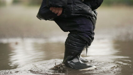 Child playing with puddle wearing rain boots