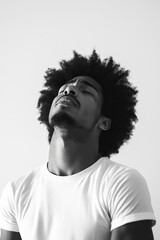 Obraz premium Black and white portrait of a man in a white t-shirt with an expressive, introspective pose looking upwards.