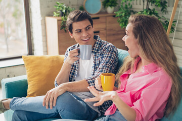 Two cheerful young friends enjoy coffee during a relaxing day at home, sharing stories and bonding in a comfortable and chic living room.