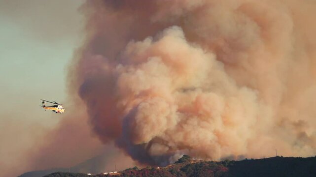 A massive and uncontrollable wildfire engulfs the mountains in Los Angeles, with helicopters and planes tirelessly battling the raging blaze, threatening houses and precious wildlife in the area