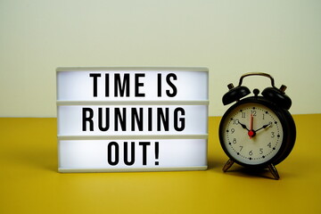 Time Is Running Out! text on LED lightbox with alarm clock on yellow background