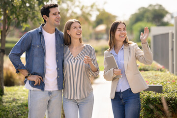 Happy young Hispanic couple and real estate agent viewing good area for living, looking away at new house, discussing rent, property buying, mortgage. Realtor showing neighborhood to customers