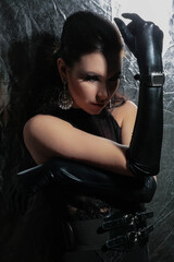 a beautiful, fashionable young brunette of tall stature, on a white background in latex gloves and a black bodysuit, stands in the studio