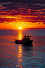 Obraz premium A boat in the ocean at sunset with the sun setting in the background