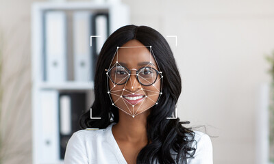 A woman with glasses smiles confidently while facial recognition technology analyzes her features. The modern office backdrop emphasizes innovation and professional atmosphere.