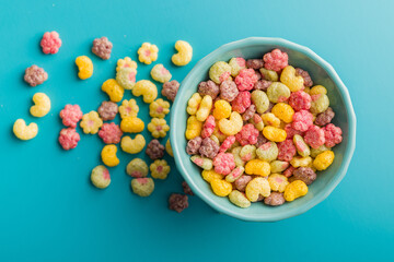 Colorful breakfast cereals in the shape of various fruit in bowl on blue background. Top view.