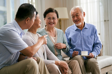 two happy senior asian couples sitting and chatting on couch at home