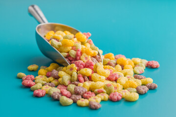 Colorful breakfast cereals in the shape of various fruit on scoop on blue background.