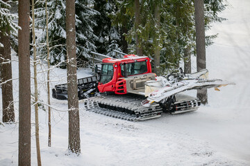 Large red snow tractor for ski slope re-tracking and snow grooming on ski slope in forest