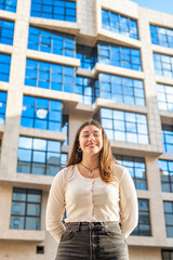 Smiling Caucasian girl in front of an office building, standing facing camera, smiling and wearing...