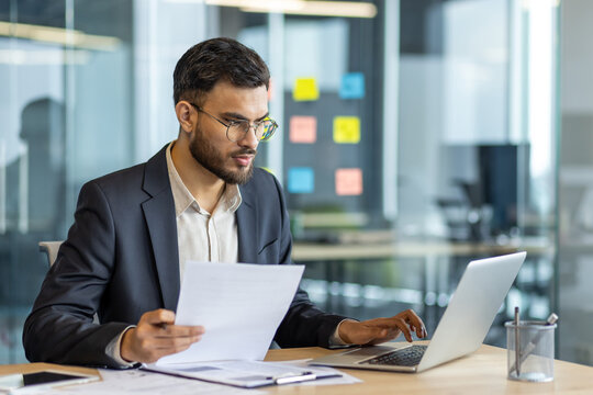 Serious focused businessman at workplace inside office. Man in business suit working with documents and papers, mature successful financier investor reviewing reports.