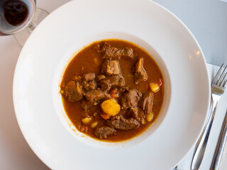 Appetizing hot beef stew in sauce served with potato slices on platter