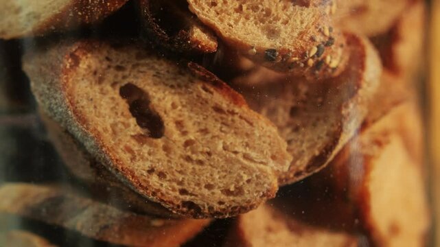 Slices of artesian bread in glass pot on bakery shop close-up. Bread with black poppy garnish on top and white flour on top. Artisan bread is making by skill
