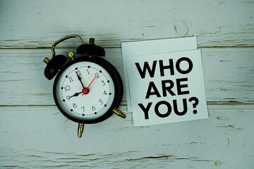 Who Are You? text message on sticky note with alarm clock on wooden background
