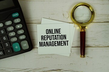 ORM (Online Reputation Management ) text message on sticky note with magnifying glass and calculator on wooden background