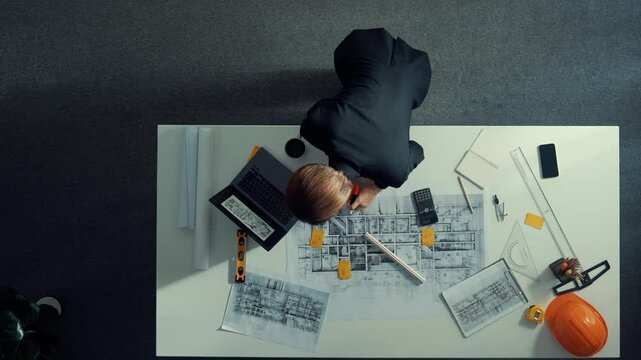 Top view of skilled project manager holding project plan and explain house design to architect engineer at meeting table with equipment, ruler, safety helmet and laptop scatter around. Alimentation.