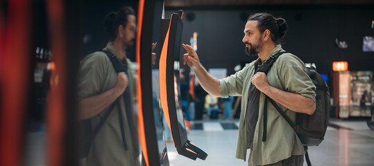 A man checks in for a plane at the electronic check-in desk. A young tourist guy at the airport gets a ticket at the check-in screen