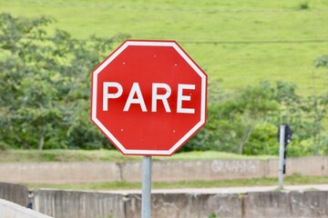 Placa de sinalização de transito na beirada de uma rodovia indicando pare na cor vermelha e fundo desfocado.
