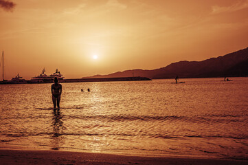Fototapeta premium Beautiful sunset with red colors on the sea with a girl coming out of the water