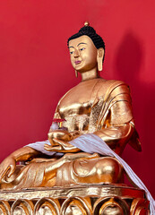 A golden statue of Buddha against a bright red wall. Detailed carvings and calm expression...