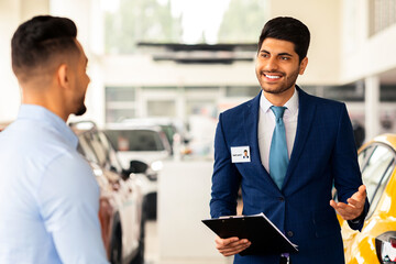 Cheerful VIP car salon manager having conversation with male customer, giving useful tips for...