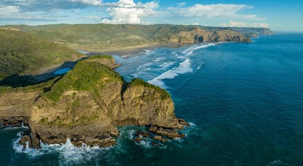 Fototapeta premium Dramatic coastal scenery. Ocean waves crash against rocky cliffs. New Zealand coastline. Bethells Beach, Auckland, New Zealand