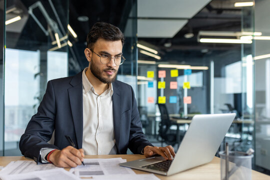 Serious thinking businessman doing paperwork inside office, man filling out paper tax forms, and signing documents and contracts. Successful financier investor preparing report.