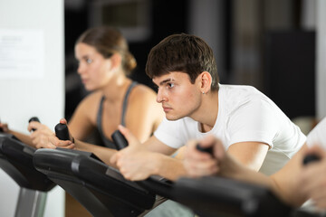 Obraz premium Guy hardly perform track on stationary bicycle, pedaling and exercising in fitness class. Fitness equipment, athlete engaged in physical task during training, work out, participate in sport challenge