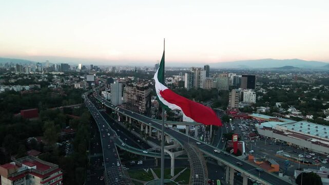 Drone footage of a huge Mexican flag waving with a view of Mexico city with buildings and traffic