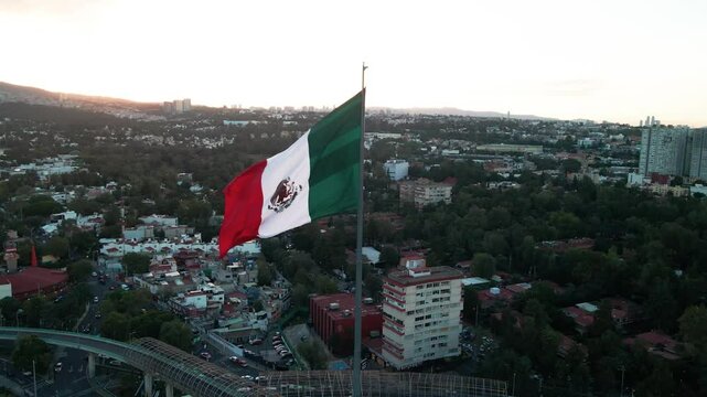 Drone footage of a huge Mexican flag waving with a view of Mexico city with buildings and traffic