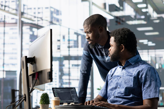 Data engineering IT staff members at PC desk developing machine learning algorithms. African american team in office solving tasks, training large scale deep learning models using computer