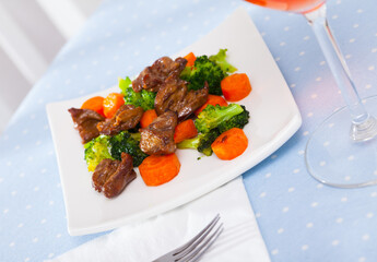 Roasted chicken hearts served with boiled broccoli and baked carrots on white plate