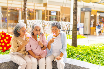 Happy Asian senior woman travel and shopping in the city on summer holiday vacation. Group of Healthy elderly women friends enjoy and fun outdoor lifestyle eating ice cream together at shopping mall.