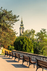 Resting place with benches on the Kalemegdan fortress wall with the Cathedral Church of Saint Michael the Archangel behind green trees